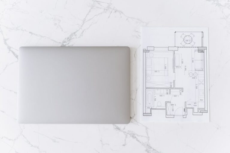 Top view of a laptop and architectural blueprint on white marble surface, showcasing modern workspace.
