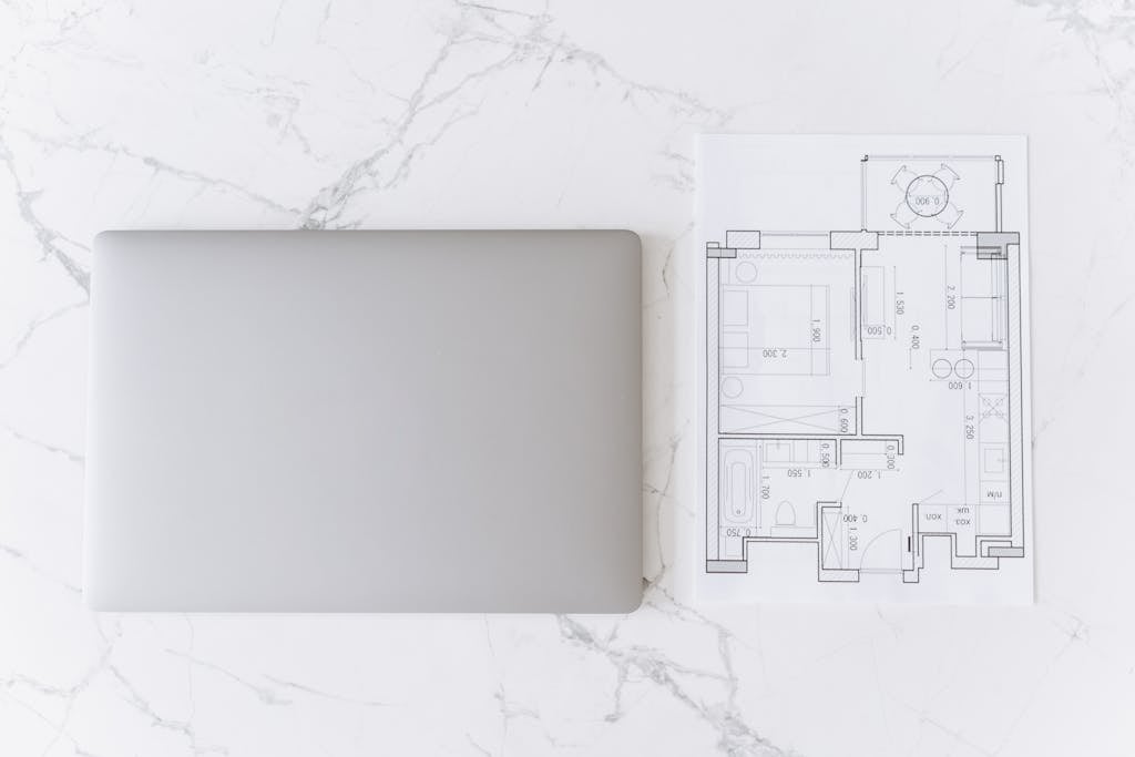 Top view of a laptop and architectural blueprint on white marble surface, showcasing modern workspace.